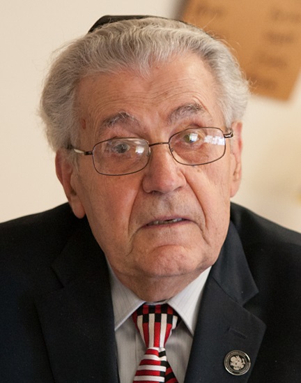 Holocaust survivor Howard Melton wearing a dark suit and striped tie, photographed at an indoor event.
