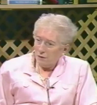 Molly Kleiner, a Holocaust survivor, speaks during a recorded interview. She has short white hair and wears a pink top with a pearl necklace.