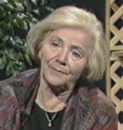 Rebecca Peltz, a Holocaust survivor, speaks during a recorded interview. She has short white hair and wears a dark floral top with a delicate necklace.