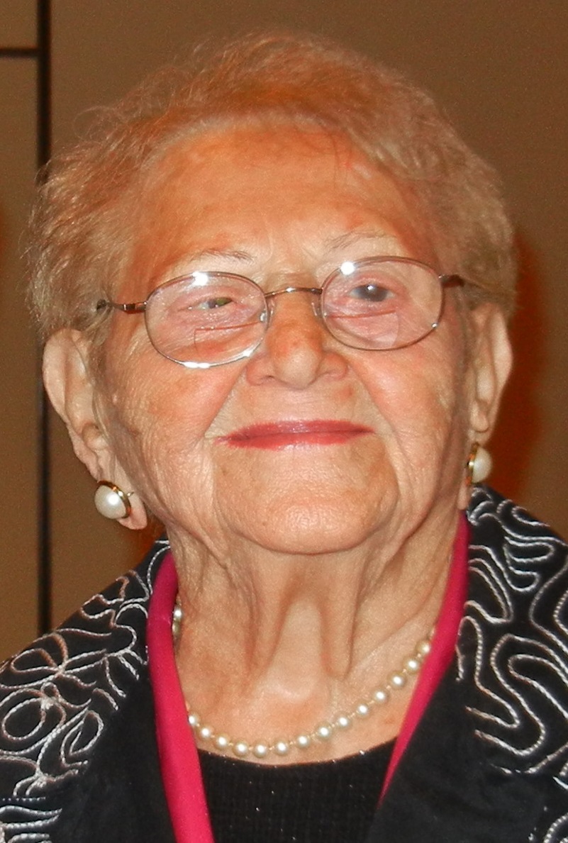Tauba Biterman, a Holocaust survivor, smiles warmly at the camera wearing wire-rimmed glasses and a black patterned top.