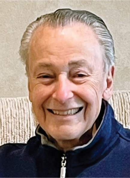 Holocaust survivor Werner Richheimer smiling warmly, wearing a navy zip-up jacket, in a close-up portrait photo.