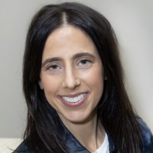 Professional headshot of a woman, Jessica Sectzer-Rubin with long dark hair, smiling at the camera. She wears a dark navy top over a white collared shirt, photographed against a light neutral background.