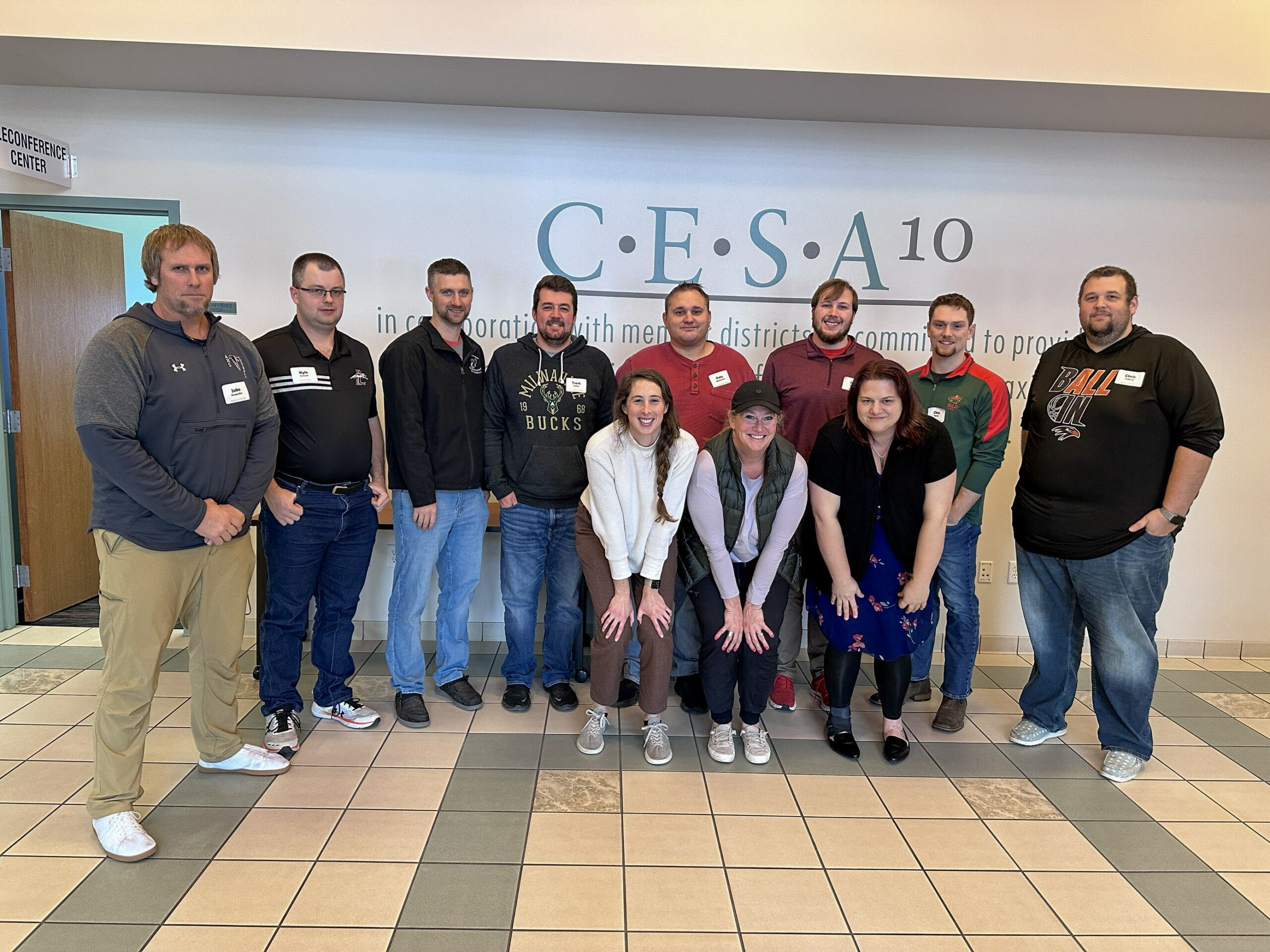 Nine educators pose for a group photo in front of a CESA 10 sign during a teacher training workshop. HERC staff members Sam Goldberg and Jennifer Koss crouch in the front left and right, alongside two workshop participants. Five additional participants stand in the back row.