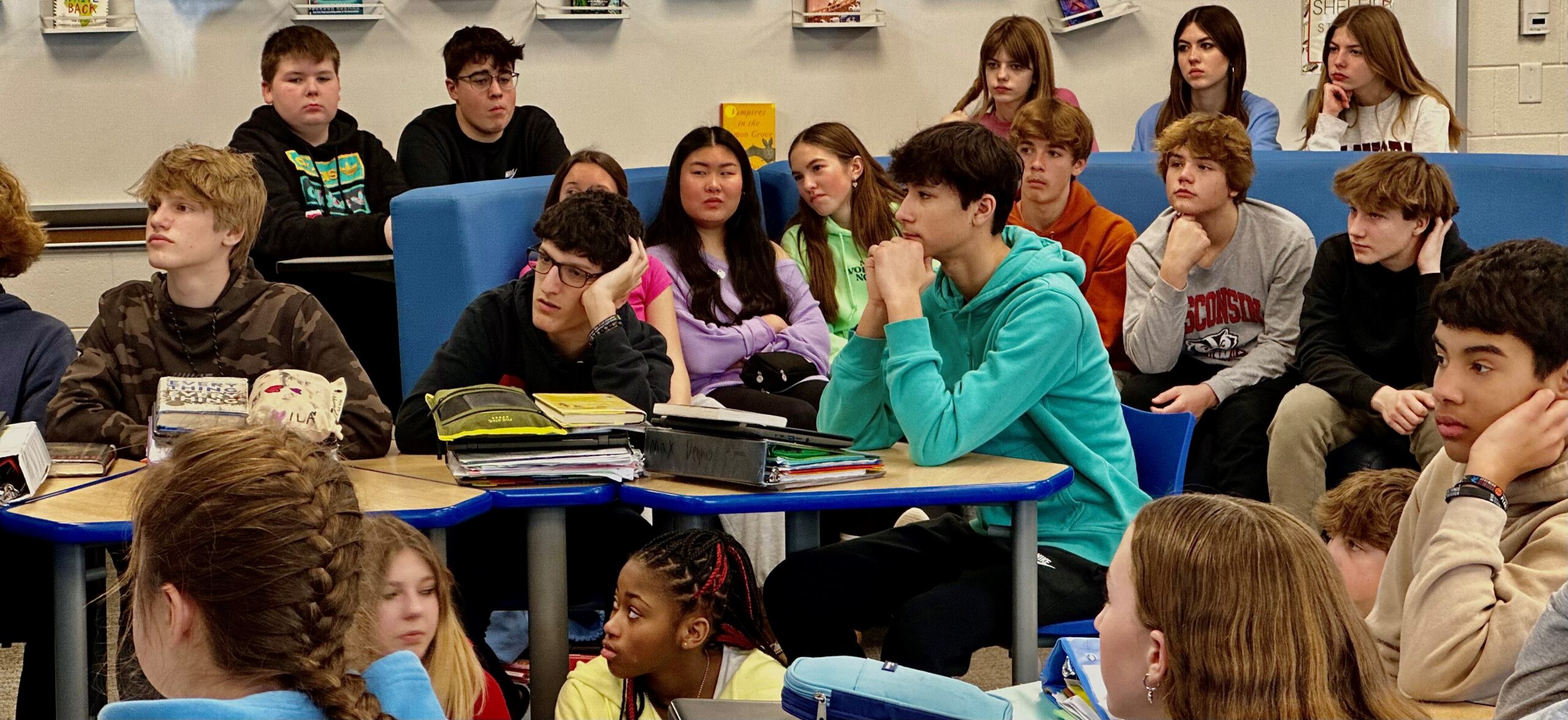 Middle school students engaged in listening during a HERC classroom workshop, seated at blue tables with focused, thoughtful expressions.
