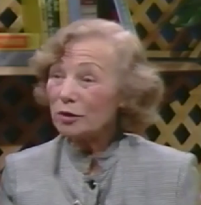 Sylvia Blasberg, a Holocaust survivor, speaks during a recorded interview. She has short white hair and wears a light gray blazer.
