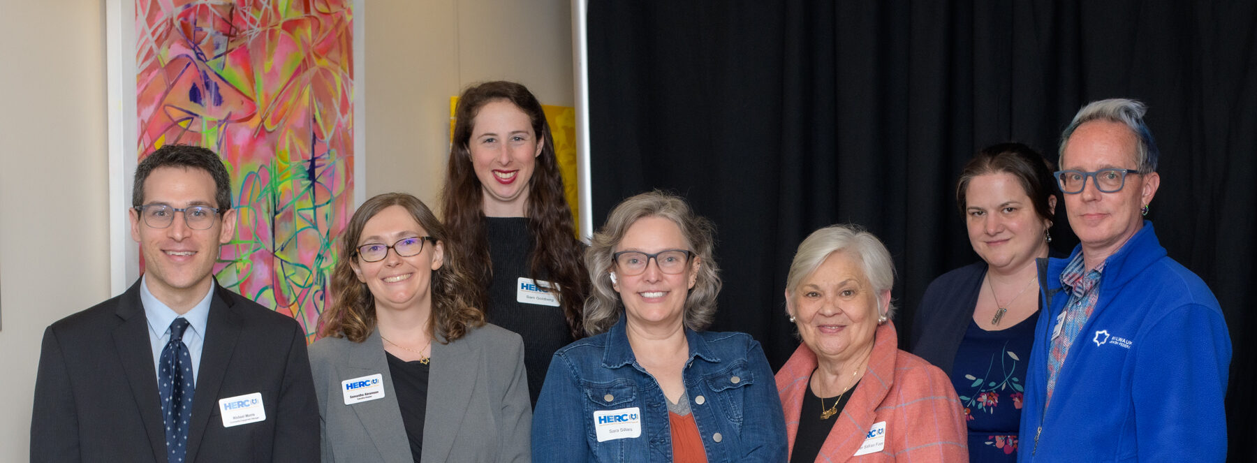 Six HERC staff members and a Yom HaShoah speaker pose together for a group photo, all smiling at the camera.