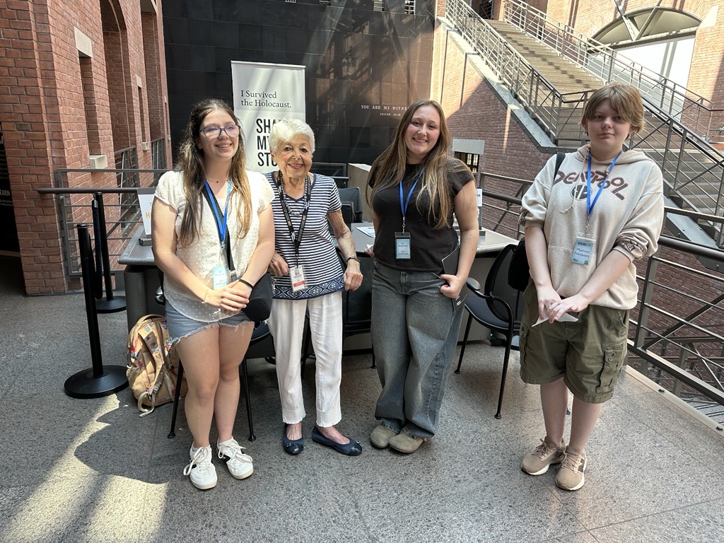 Three teenagers stand with an older woman posing for picture.
