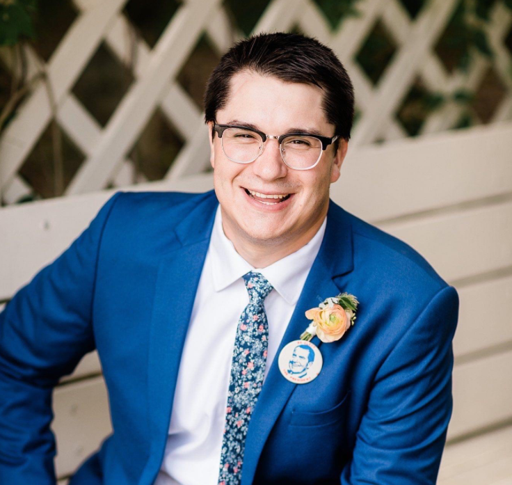 Man with dark hair in a blue suit smiles at camera