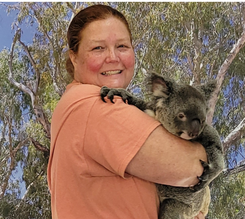 A woman in an orange shirt faces the camera while holding a koala.
 